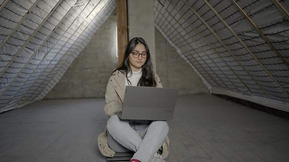 Energieberaterin Özlem Özdemir-Bierhoff sitzt mit einem Laptop auf dem Boden eines Dachgeschosses.