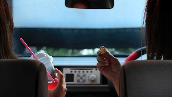 Zwei Freundinnen mit Popcorn sitzen im Auto, während sie sich einen Film auf einer Leinwand ansehen. 