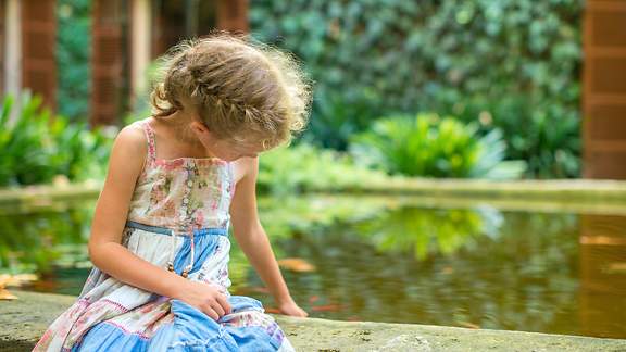 Kleines Mädchen sitzt am Teich