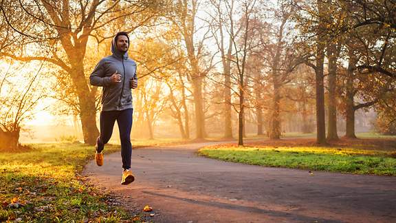 Ein Mann joggt im Morgengrauen durch einen Park