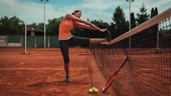 Junge Frau deht ihre Beinmuskulatur auf dem Tennisplatz