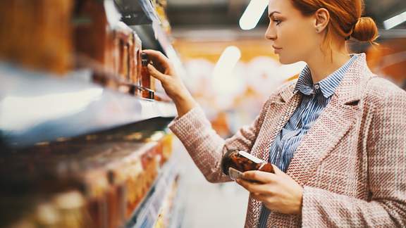 Eine Frau steht mit prüfendem Blick vor einem Supermarktregal