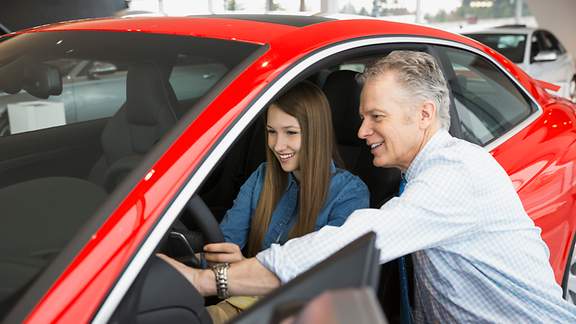 Junge Frau lässt sich im Showroom von einem Verkäufer ein rotes Auto zeigen