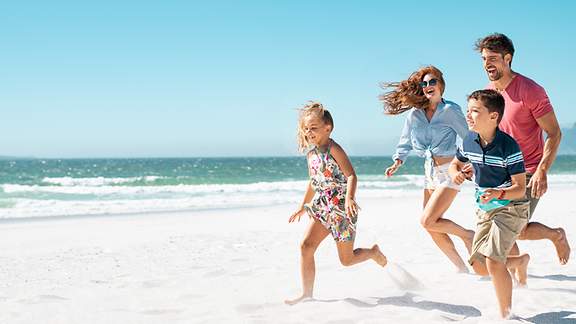 Familie mit zwei jungen KIndern läuft fröhlich am Strand entlang