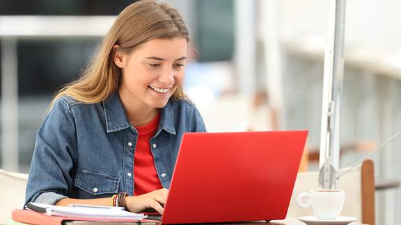 Glückliche Schülerin blickt auf ihren roten Laptop